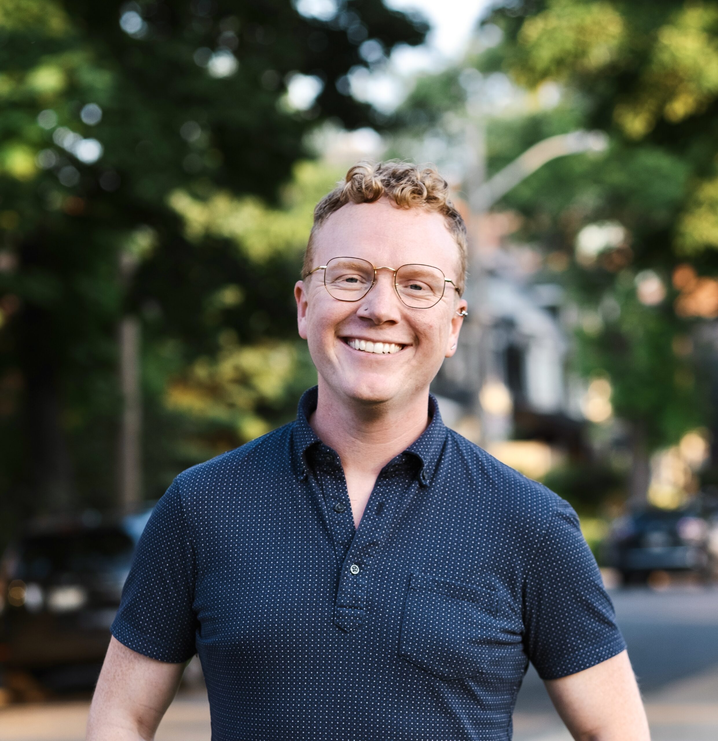 A headshot of Dr. Alex Wells smiling on a sunny street.