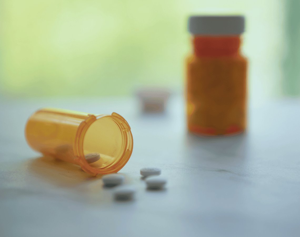 Two bottles of aspirin, one lying on its side with pills streaming gout. 